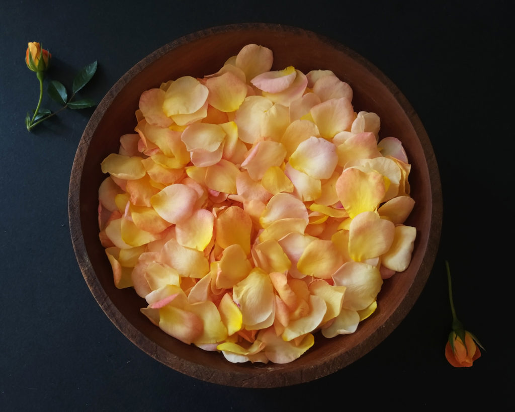 A pile of sunset rosepetals rests in a handmade wooden bowl.