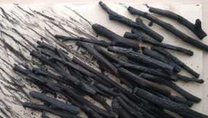 Handmade apple-wood charcoal sticks drawing burnt lines on the surface of a delicate rice paper.