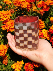 My hand holds a patterned ceramic cup above a dense cloud of marigold flowers in early autumn.