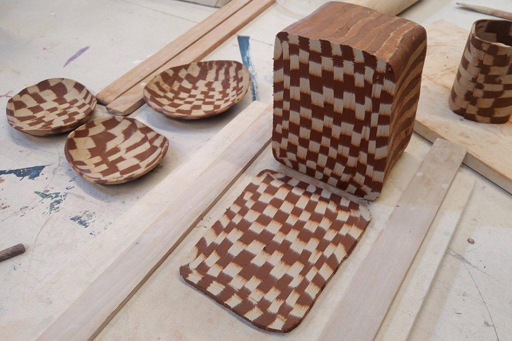 A large block of patterned clay sits on the table. Several small bowls made of patterned clay dry nearby.