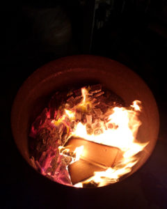 A large metal barrel loaded with ceramics and firewood burning steadily in the darkness.