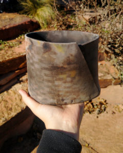 My hand is holding a ceramic vase with mysterious burns and smoke marks from the barrel firing.