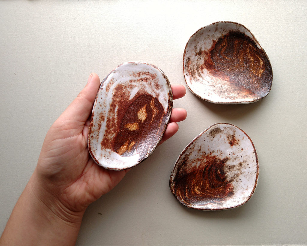 Three oval shaped ceramic dishes. They are a swirl of contrasting clays with a rim of smooth white glaze.