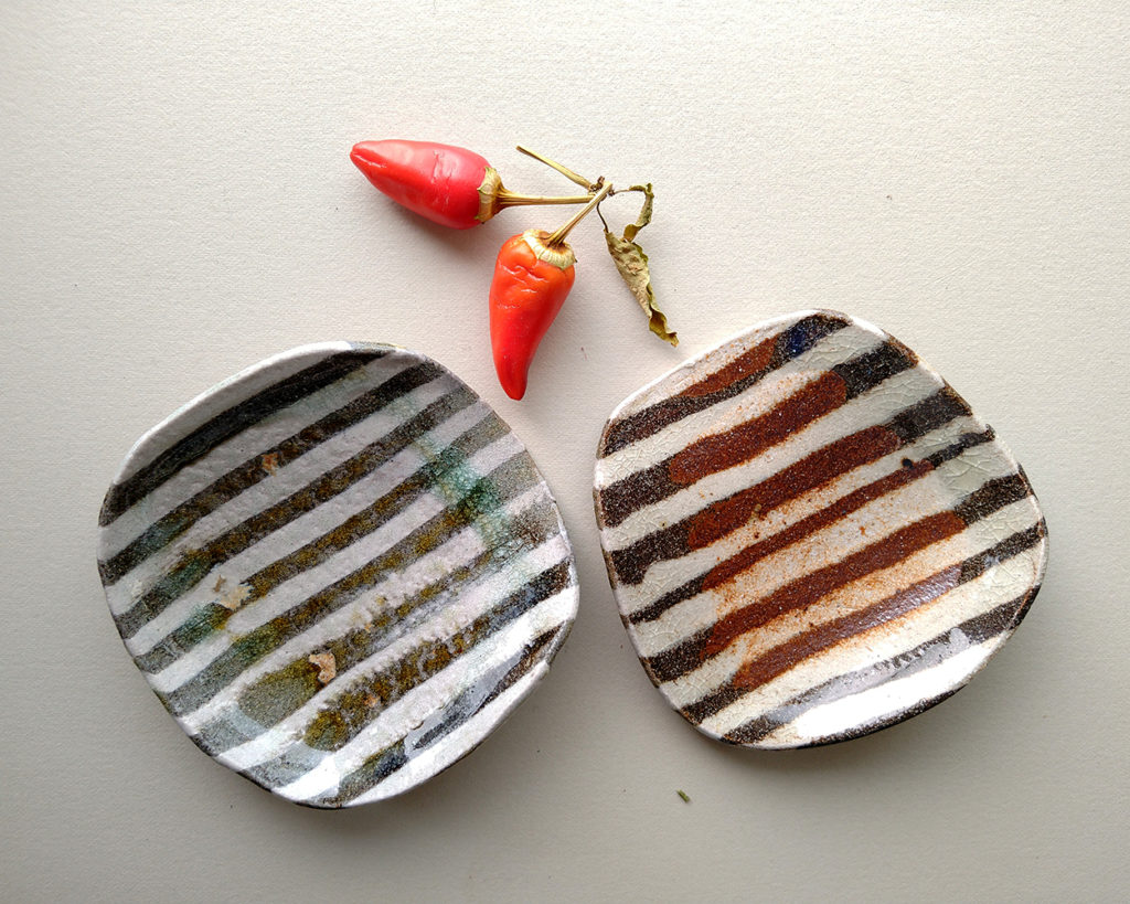 Two small, soft, hot peppers rest near two small dishes with a contrasting nerikomi stripe pattern