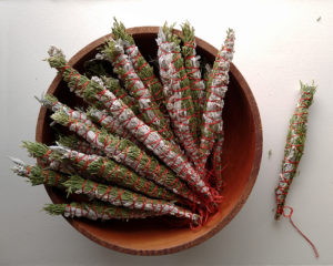 Small bundles made of juniper branches and artemisia stems are stacked in a shallow wood bowl.