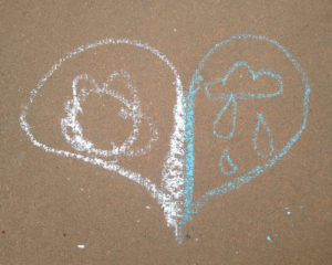 A heart shape drawn on the sidewalk with chalk. It is split in half, one side holds a flower and the other holds a cloud raining large drops.