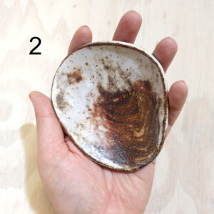 Artist Isa Rodriguez's hand holding a small rounded dish with a brown and white marble pattern on it.