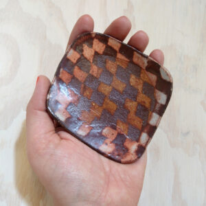 Artist Isa Rodriguez's hand holding a small square dish with a red and white checker pattern on it.