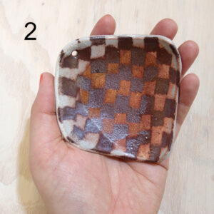 Artist Isa Rodriguez's hand holding a small square dish with a red and white checker pattern on it.