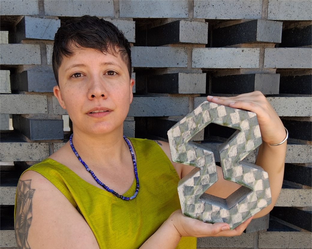 Artist Isa Rodriguez stands in front of a brick wall holding a ceramic sculpture. The piece was created at their 2025 Studio School residency.